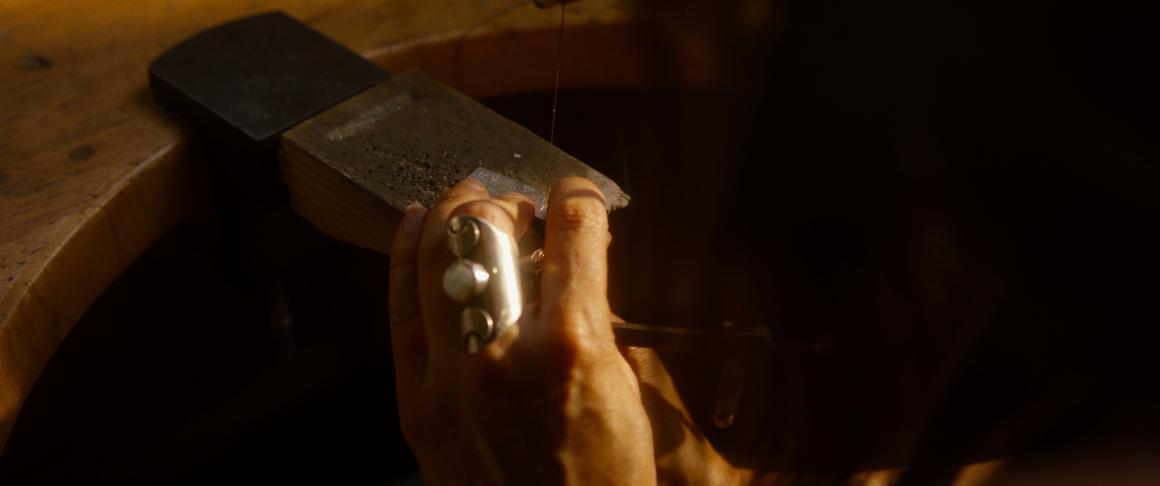 Main portant une bague avec motifs de lune et pierre blanche en train de travailler sur une cheville de meuble de joaillerie